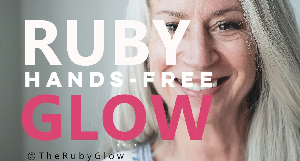 a woman with long grey hair smiles happily with words Ruby Glow hands-free across her face