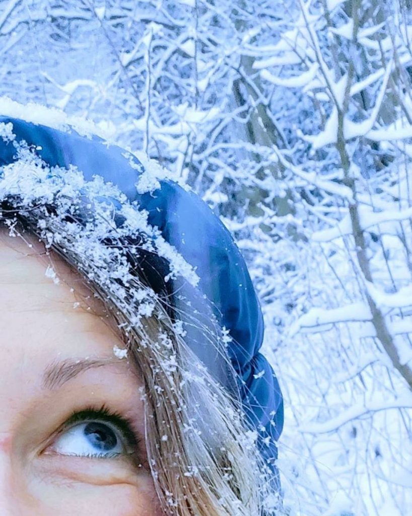 Close up of Tabitha - one eye looking up to the sky - snowflakes dusting a blue hat and snow in background