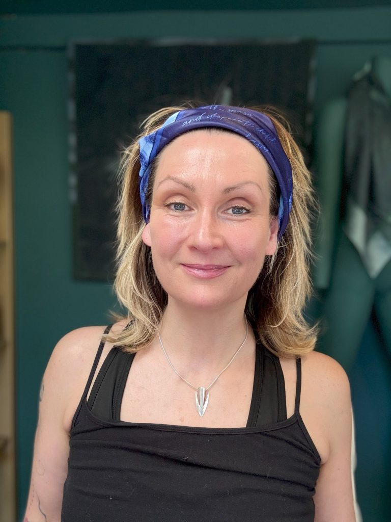 Tabitha Rayne a white scottish woman wears a blue scarf with a nude on it tastefully folded so as not to offend holding her hair off her glowing face for masturbation month